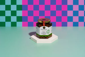 A jar of mandarin infused olives sitting on a white disc with a checkerboard coloured background. 