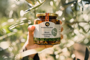A jar of olives being held up against an olive tree.